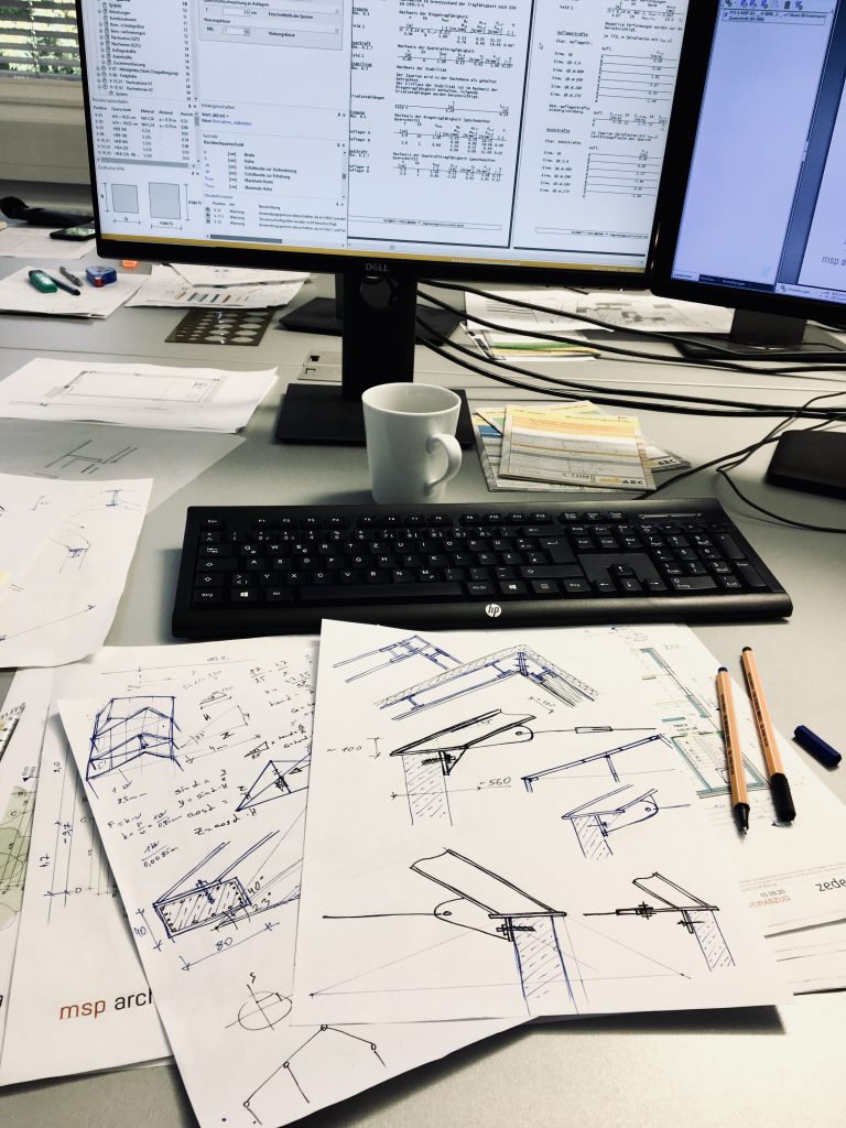Arbeitsplatz mit Bildschirm, Tragwerksplänen und Handskizzen
